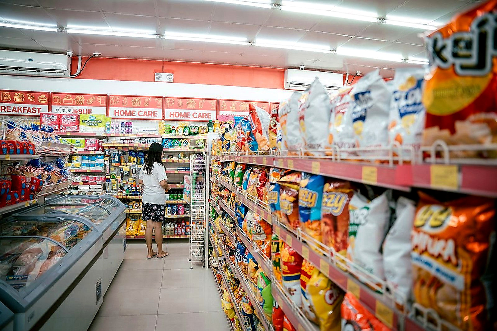 Free A woman browsing snack shelves at a supermarket, surrounded by various chips packages. Stock Photo